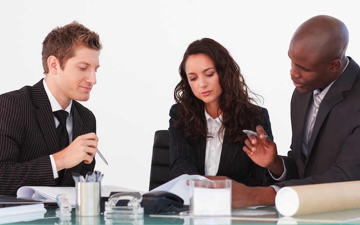 Three colleagues reviewing papers across a meeting table